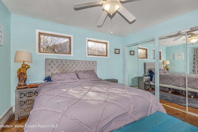 bedroom featuring a baseboard heating unit, ceiling fan, wood finished floors, and two closets