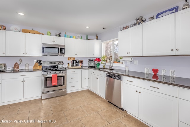 kitchen featuring dark stone countertops, white cabinetry, appliances with stainless steel finishes, and a sink