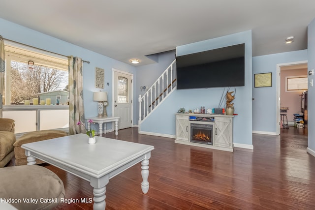 living area with dark wood-style floors, a warm lit fireplace, baseboards, and stairs