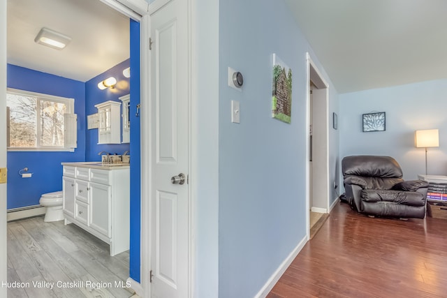 hall with baseboard heating, light wood-type flooring, and baseboards