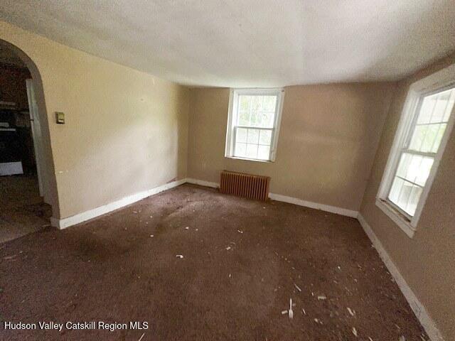 818 Cauterskill Rd, Catskill, NY 12414 - empty room featuring radiator heating unit, arched walkways, baseboards, and carpet floors