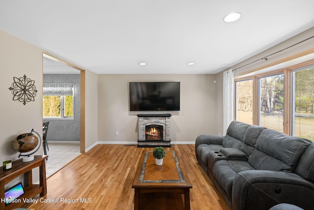 living area with a stone fireplace, baseboards, light wood finished floors, and recessed lighting