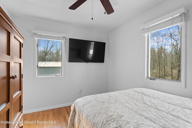 bedroom with baseboards, multiple windows, ceiling fan, and light wood-style floors