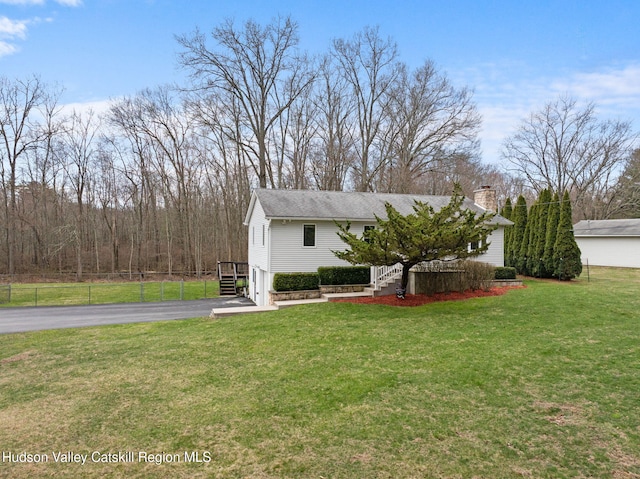 view of front of property featuring aphalt driveway, fence, and a front lawn