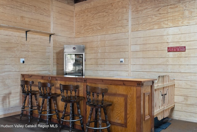 bar featuring a bar, wood walls, and baseboards
