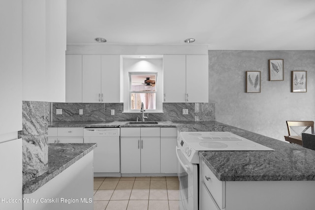 kitchen with dark stone counters, white appliances, a peninsula, white cabinetry, and a sink