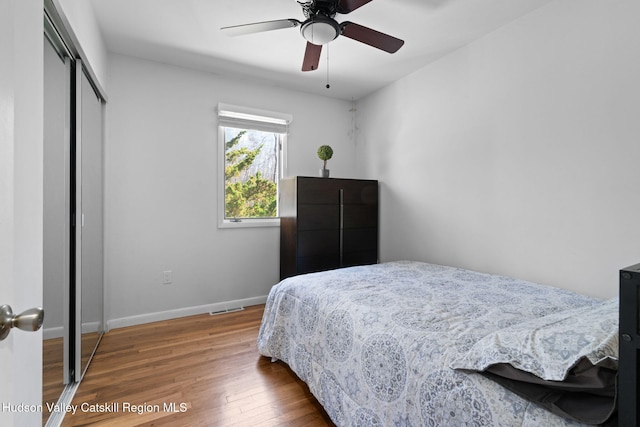 bedroom with visible vents, a closet, baseboards, ceiling fan, and wood finished floors