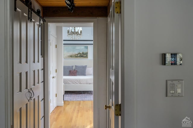 corridor featuring light wood-style flooring, a barn door, and a chandelier