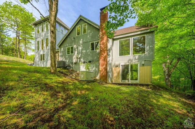 back of property featuring a chimney, a lawn, and central AC unit