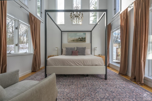 bedroom featuring a chandelier, multiple windows, wood finished floors, a towering ceiling, and baseboards