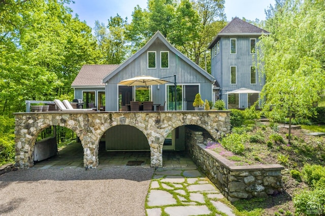back of house featuring a shingled roof and stone siding