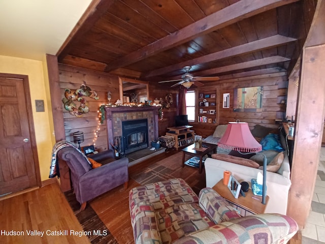 living room featuring ceiling fan, wooden walls, a tile fireplace, beam ceiling, and hardwood / wood-style floors