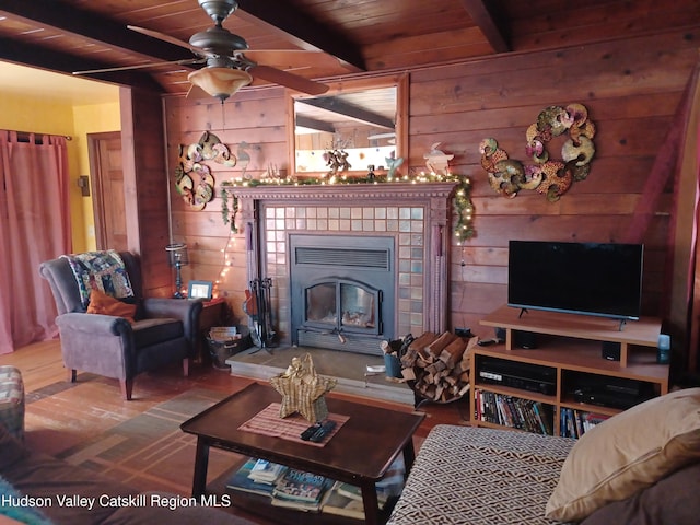 living room featuring beam ceiling, a tile fireplace, wood walls, and wood ceiling