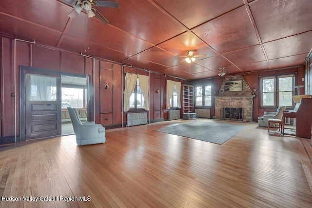 996 Dominican Ln, Saugerties, NY 12477 - unfurnished living room featuring ceiling fan, wood-type flooring, a stone fireplace, plenty of natural light, and a decorative wall