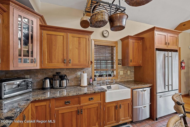 kitchen featuring vaulted ceiling, sink, backsplash, dark stone counters, and stainless steel appliances