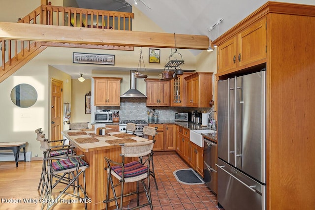 kitchen featuring high quality appliances, sink, a kitchen breakfast bar, decorative backsplash, and wall chimney exhaust hood