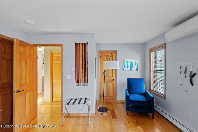 living area with baseboard heating, a wall unit AC, and light hardwood / wood-style flooring