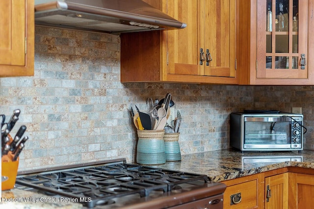 kitchen featuring dark stone countertops, backsplash, ventilation hood, and stove