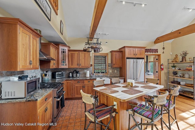 kitchen featuring sink, backsplash, premium appliances, lofted ceiling with beams, and a kitchen bar