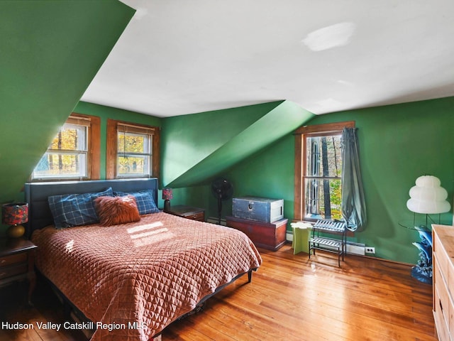 bedroom with a baseboard radiator, light hardwood / wood-style flooring, and multiple windows