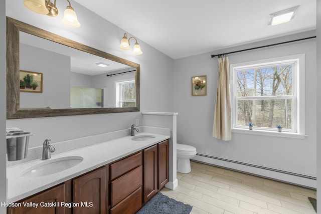 full bath with double vanity, baseboard heating, a sink, and toilet