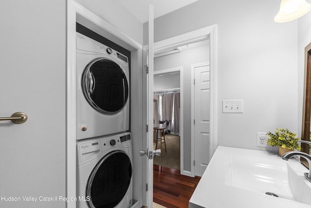 laundry area with dark wood-style flooring, a sink, and stacked washer and clothes dryer