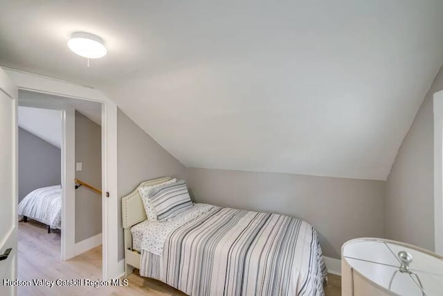 bedroom featuring lofted ceiling, baseboards, and light wood-type flooring