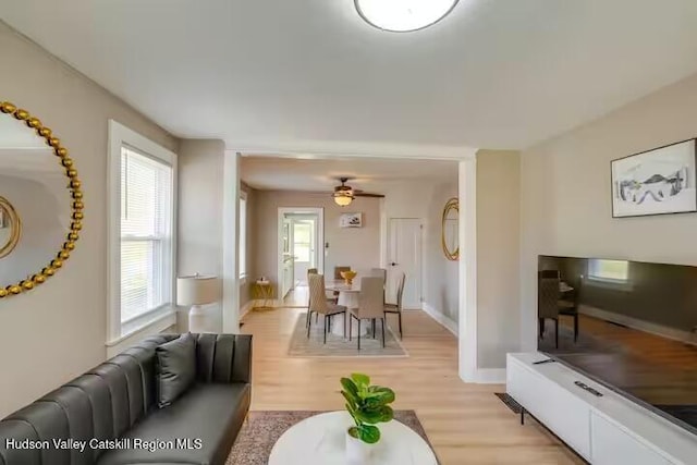 living area with light wood-style flooring, plenty of natural light, baseboards, and a ceiling fan