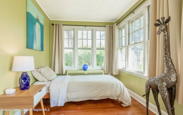 bedroom with wood-type flooring, radiator heating unit, and crown molding