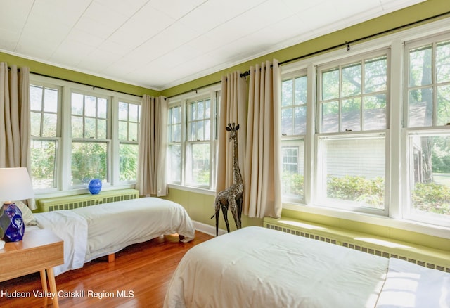 bedroom with radiator heating unit, ornamental molding, and hardwood / wood-style flooring