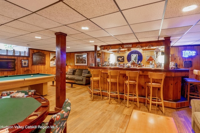 bar with wood walls, a drop ceiling, and hardwood / wood-style flooring