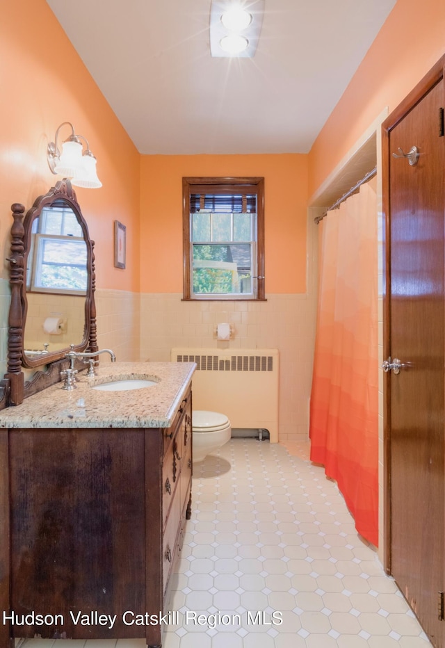 bathroom featuring radiator, vanity, tile walls, and toilet