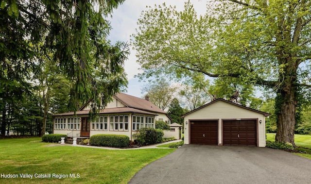 view of front of home featuring a front yard, a garage, an outdoor structure, and a sunroom