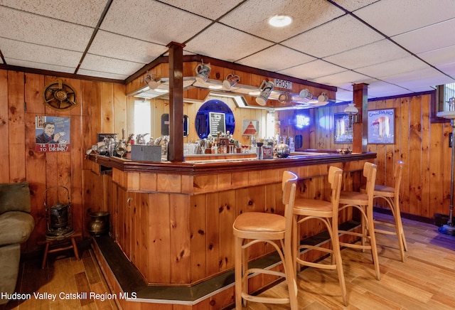 bar with a drop ceiling, wooden walls, and light hardwood / wood-style flooring