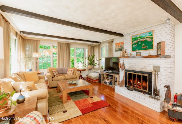 living room featuring beam ceiling, wood-type flooring, and a brick fireplace