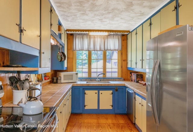 kitchen featuring tile counters, sink, light hardwood / wood-style floors, a textured ceiling, and appliances with stainless steel finishes