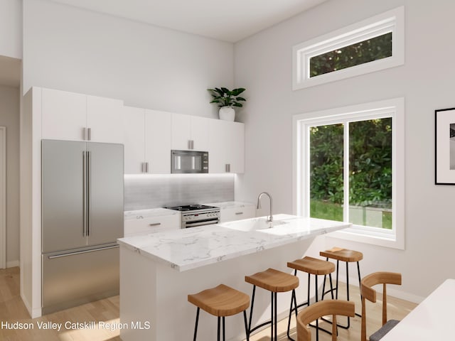 kitchen with white cabinetry, sink, stainless steel appliances, light hardwood / wood-style floors, and a kitchen bar