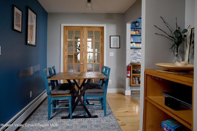 dining room with a baseboard heating unit, baseboards, french doors, and wood finished floors