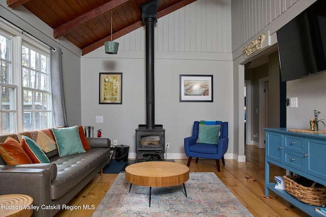 living area featuring a wood stove, beam ceiling, wood ceiling, light wood-style flooring, and high vaulted ceiling