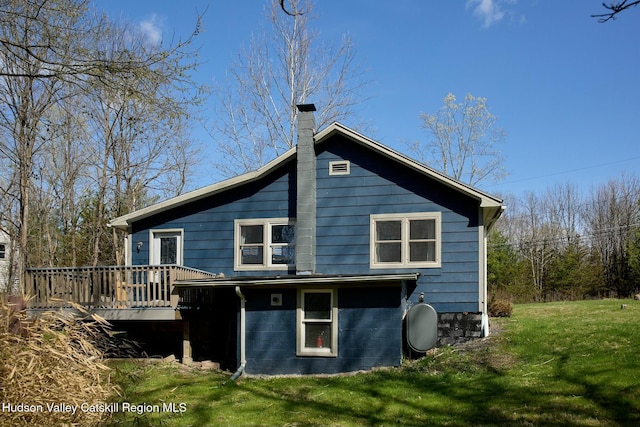 rear view of property with a chimney, a deck, and a lawn