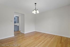spare room featuring a chandelier, light wood finished floors, and baseboards