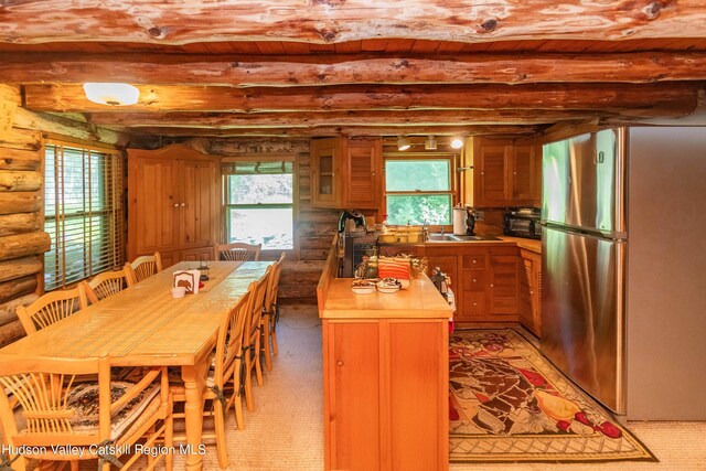 carpeted dining room featuring beam ceiling, rustic walls, and plenty of natural light