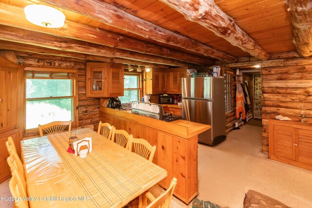 kitchen featuring beamed ceiling, a healthy amount of sunlight, kitchen peninsula, and stainless steel refrigerator