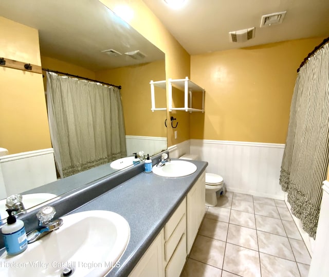 full bath with a wainscoted wall, double vanity, a sink, and visible vents