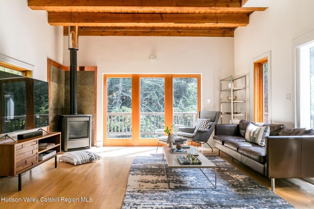 living room with beamed ceiling, a towering ceiling, light hardwood / wood-style floors, and a wood stove