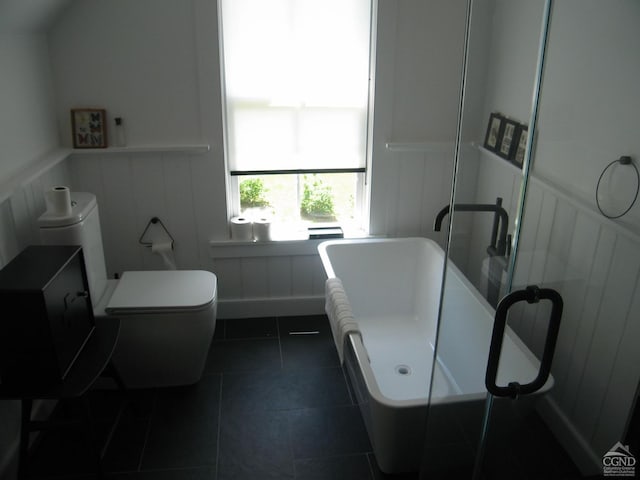 bathroom featuring wainscoting, a freestanding tub, toilet, a decorative wall, and tile patterned floors