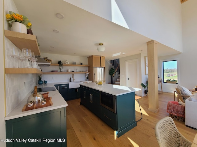 kitchen with decorative columns, a kitchen island, built in microwave, sink, and stainless steel refrigerator