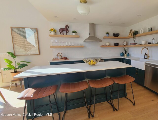 kitchen with a kitchen breakfast bar, appliances with stainless steel finishes, wall chimney exhaust hood, sink, and light hardwood / wood-style floors