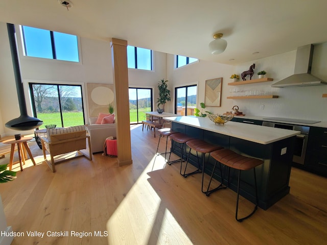 kitchen with wall chimney range hood, light wood-type flooring, a kitchen bar, a kitchen island, and electric stovetop