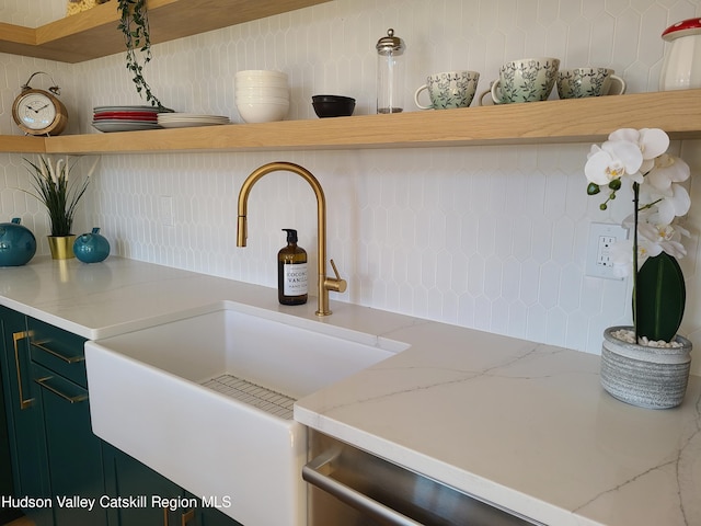 kitchen with tasteful backsplash, green cabinets, light stone counters, and sink